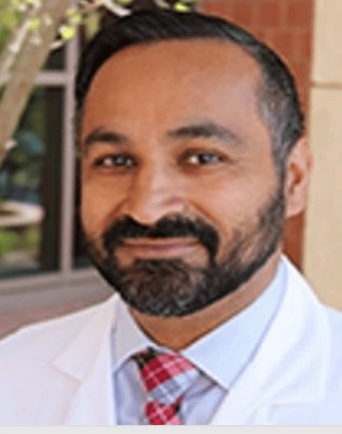 Person wearing a white coat and red plaid tie, standing outdoors.