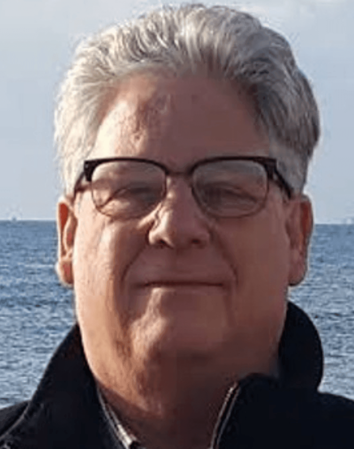 Person with grey hair standing by the ocean on a clear day.